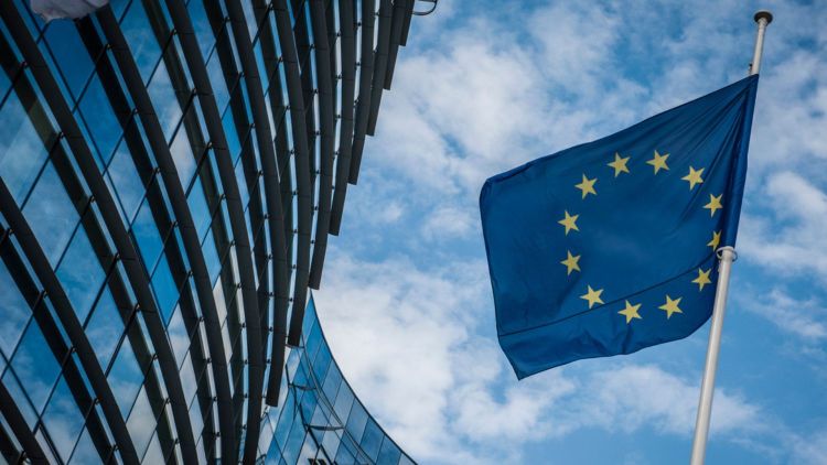 ES karogs mastā, kas atrodas blakus ēkai ar stiklotu fasādi